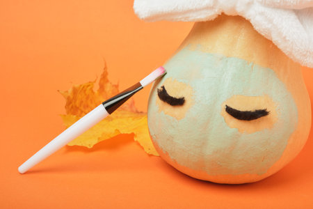 Autumn pumpkin with clay mask in white cosmetic bandage on orange background, brushes for applying mask, copy space, mock upの写真素材