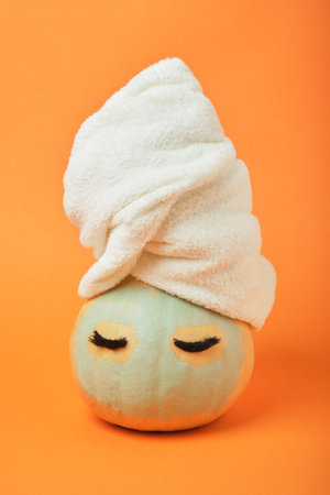 A pumpkin with eyes and a white terry towel on its head, a blue clay mask on its face, an orange backgroundの写真素材