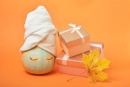 A pumpkin smeared with clay with a towel on top and gift boxes on an orange background, the time for holiday gifts and sales conceptの写真素材