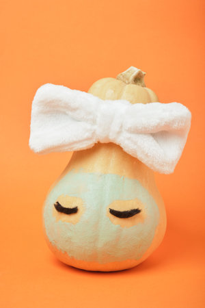 Autumn pumpkin with clay mask in white bandage on orange background, copy space, mock upの写真素材