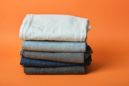 a stack of jeans of different colors on an orange background