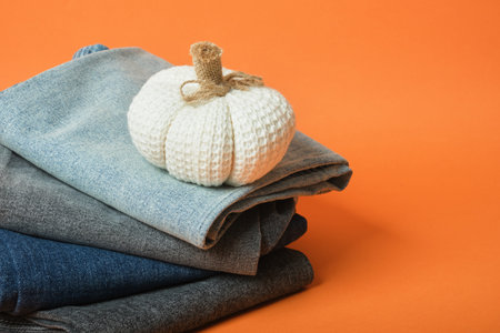 Decorative pumpkin and stack of jeans of different colors on orange background, autumn clothing sale conceptの写真素材