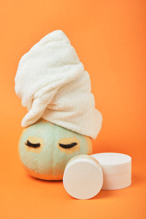 Mock-up jars of cream and yellow pumpkin in a clay mask and a towel on the head Natural organic spa cosmetics concept. Vitamin intense seed of pumpkin cream concept.の写真素材