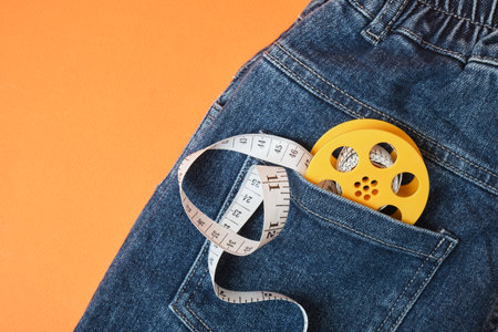 Measuring tape and jeans on an orange background, the concept of fighting excess weight in the autumn periodの写真素材