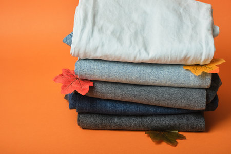 Stack of jeans of different colors on orange background, autumn clothing concept