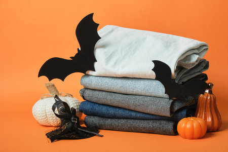 Halloween decor and a stack of jeans of different colors on an orange background, autumn sale of Halloween clothesの写真素材