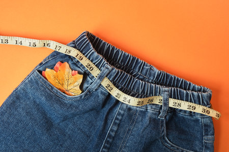 Measuring tape and jeans on an orange background, the concept of fighting excess weight in the autumn periodの写真素材