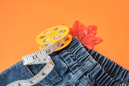 Measuring tape and jeans on an orange background, the concept of fighting excess weight in the autumn periodの写真素材