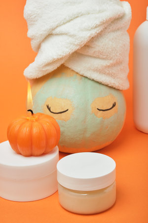 Mock-up jars of cream and yellow pumpkin in a clay mask and a towel on the head Natural organic spa cosmetics concept. Vitamin intense seed of pumpkin cream concept.の写真素材