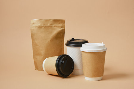 Various cardboard takeaway coffee cups and zip-lock paper bag mock-ups, coffee beans in packaging, beige backgroundの写真素材