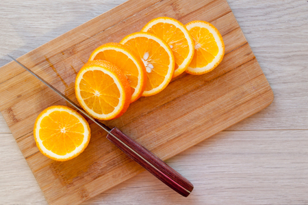 Slice of orange on wooden board with sharp knife. Fresh citrus orange fruits on cutting board for salad or juicing. Healthy eating, cooking, diet and summer concept.の写真素材