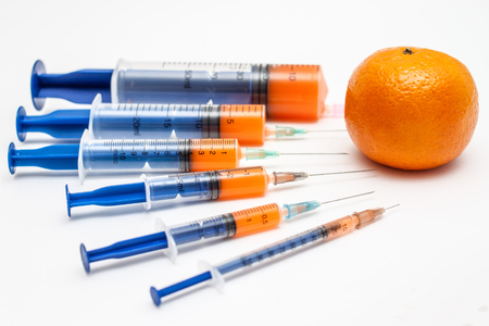 Medical syringes full of vitamin juice and a mandarin fruit for a healthy lifestyleの写真素材