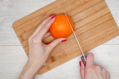 Hand slicing ripe orange on wooden board. Woman young housewife in kitchen at home slicing orangeの写真素材