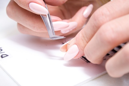 Beauty and fashion concept - Eyelash Extension Procedure. Woman hands Closeup with tool for eyelash...