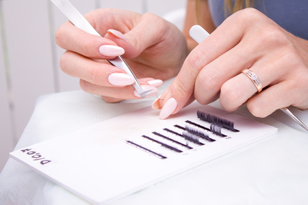 Beauty and fashion concept - Eyelash Extension Procedure. Woman hands Closeup with tool for eyelash extension. Master of tweezers is working.の写真素材