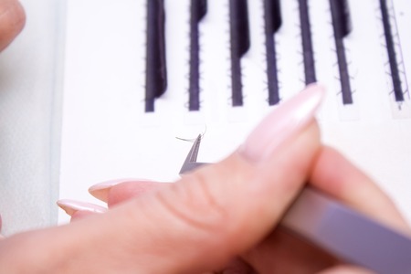 Beauty and fashion concept - Eyelash Extension Procedure. Woman hands Closeup with tool for eyelash...