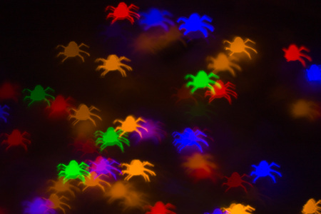 defocused bokeh multicolor lights in shape of spiders for halloween background - holidays, decoration and party conceptの写真素材