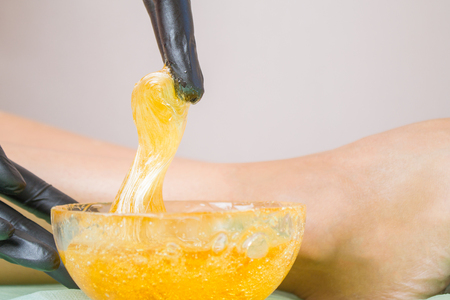 depilation and beauty concept - sugar paste or wax honey for hair removing, legs beautiful girl and hands in black glovesの写真素材