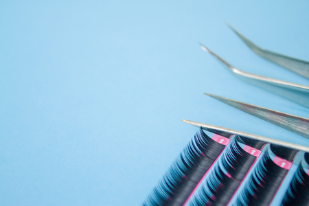 Beauty and fashion concept - tools for Eyelash Extension Procedure. Two tweezers with artificial black lashes on blue background. copyspace mockupの写真素材