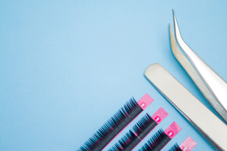 Beauty and fashion concept - tools for Eyelash Extension Procedure. Two tweezers with artificial black lashes on blue background. copyspace mockupの写真素材