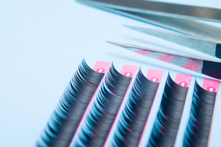 Beauty and fashion concept - tools for Eyelash Extension Procedure. Two tweezers with artificial black lashes on blue background. copyspace mockupの写真素材