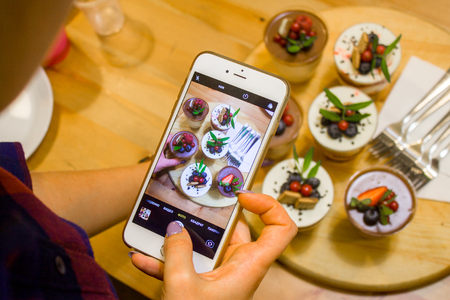 Woman hand holding phone taking photo of tasty Cupcakes with berries.  photography blogging and...
