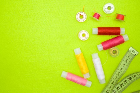 Multicolored thread coils red pink yellow white and measuring tape on green background. Sewing...