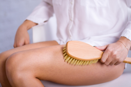 Cosmetology, grooming, Spa cosmetic products, beauty and bikini concept. closeup Woman in white makes massage legs with wooden soft massage brush for body and legs.の写真素材