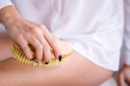 Cosmetology, grooming, Spa cosmetic products, beauty and bikini concept. closeup Woman in white makes massage legs with wooden soft massage brush for body and legs.の写真素材