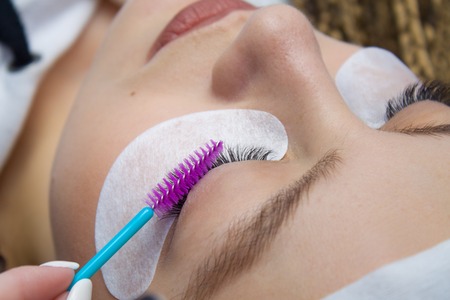 Eyelash Extension Procedure. Woman Eye with Long false Eyelashes. Close up macro shot of tweezers in hands of beauticanの写真素材