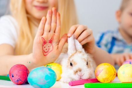 Little rabbit bunny with Colorful eggs and markers on table. blonde girl and boy on background. Prepearing for Easter, family and holidays conceptの写真素材
