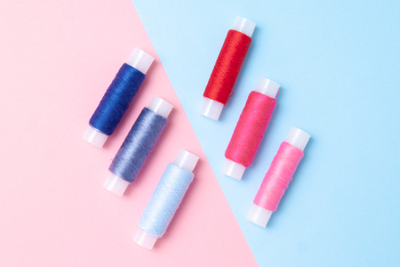 Multicolored thread coils on pink blue background. Sewing supplies and accessories for needlework,...
