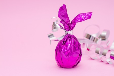 Easter greeting card with candies colored purple egg bunny ears on pink serpentine background....