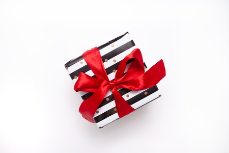 Gift or present box in white and black stripes with a red ribbon bow isolated on white table top view. Minimal flat lay composition for sales, birthday, mother day or christmas. copyspace.の写真素材