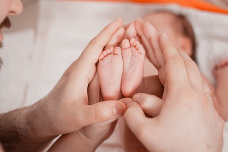 Pregnancy, maternity, preparation and expectation motherhood, giving birth concept. Newborn baby feet closeup in parents handsの写真素材