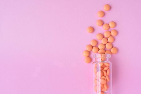 Orange tablets from glass bottle on pink background. copyspace for text. Epidemic, painkillers, healthcare, treatment pills and drug abuse concept. flat lay. top view.の写真素材