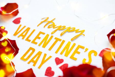 Happy Valentines Day gold text greeting card with red rose petals and shiny hearts bokeh on white wooden Background. romantic and Love concept.の写真素材