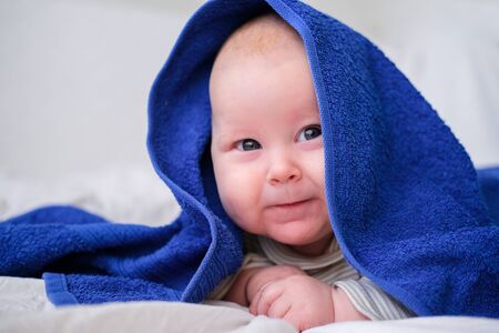 Bath time. Cute smiling caucasian infant baby looking at camera in blue towel after bathing in the...