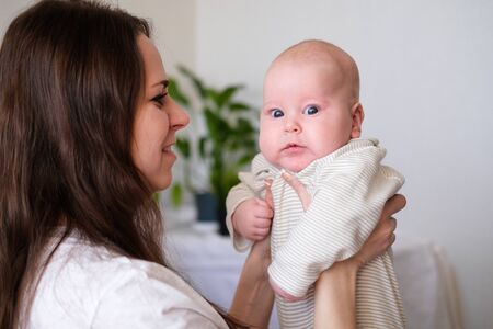 Happy baby. Little cutest serious caucasian white infant child looking at camera on mother hands....