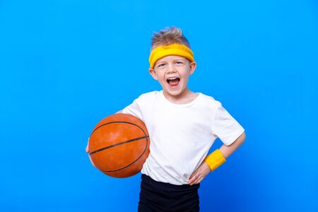 Sporty little boy with basketball ball over blue studio background. Gym workout. Child sportsman. Activity. Sport. Fitness, health and energy. Success.の写真素材
