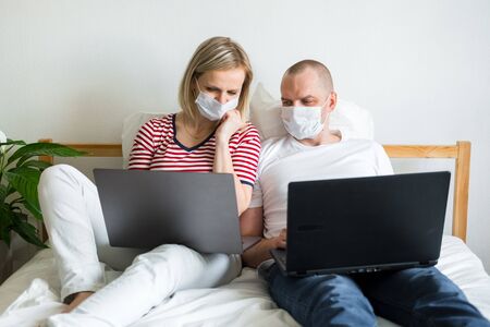 young family works remotely from home on bed at the computer. Quarantined couple coronavirus in...