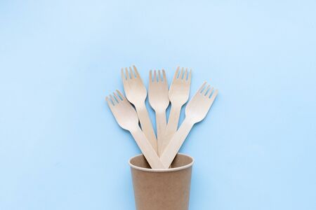 eco friendly disposable kitchenware utensils on blue background. wooden forks and spoons in paper cup. ecology, zero waste concept. top view. flat lay.の写真素材