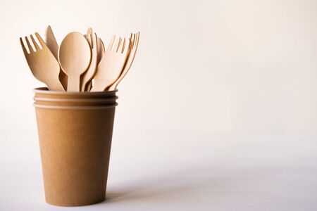 eco friendly disposable kitchenware utensils on white background. wooden forks and spoons in paper...