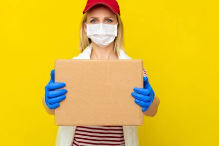 Delivery girl in red cap white t-shirt uniform face medical mask gloves hold empty cardboard box on...