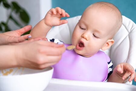 baby food. Mom feeds little caucasian child. healthy porridge, mother hands with spoon. Newborn...