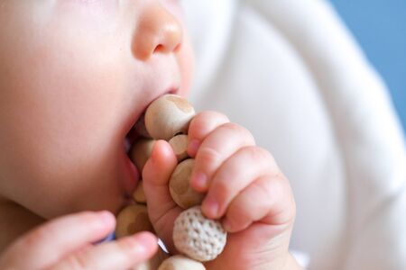 eco wood toys. baby game. Little clever caucasian child playing natural toys on highchair. games for early development. Toy in kids mouth close upの写真素材