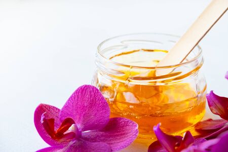 depilation and beauty concept - sugar paste or wax honey for hair removing with wooden waxing spatula stick in jar on flower backgroundの写真素材