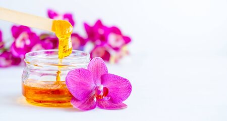 banner depilation and beauty concept - sugar paste or wax honey for hair removing flows down from wooden waxing spatula sticks on flower backgroundの写真素材