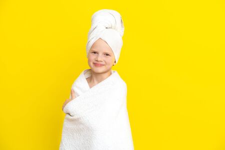 Portrait of cute little caucasian girl wrapped in white towel with bath towel on head over yellow studio background. Spa procedure, bath textile.の写真素材