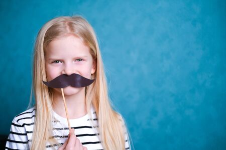 funny child blonde girl with mustache on blue background. Copyspace. Happy father dayの写真素材